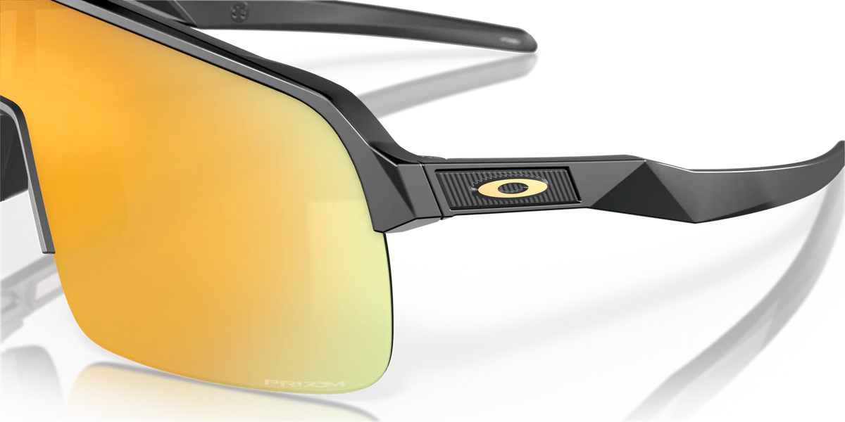 Gros plan sur les lunettes Oakley Sutro Lite Matte Carbon Prizm 24K, mettant en évidence le logo Oakley, la monture gris carbone et les reflets dorés des verres.